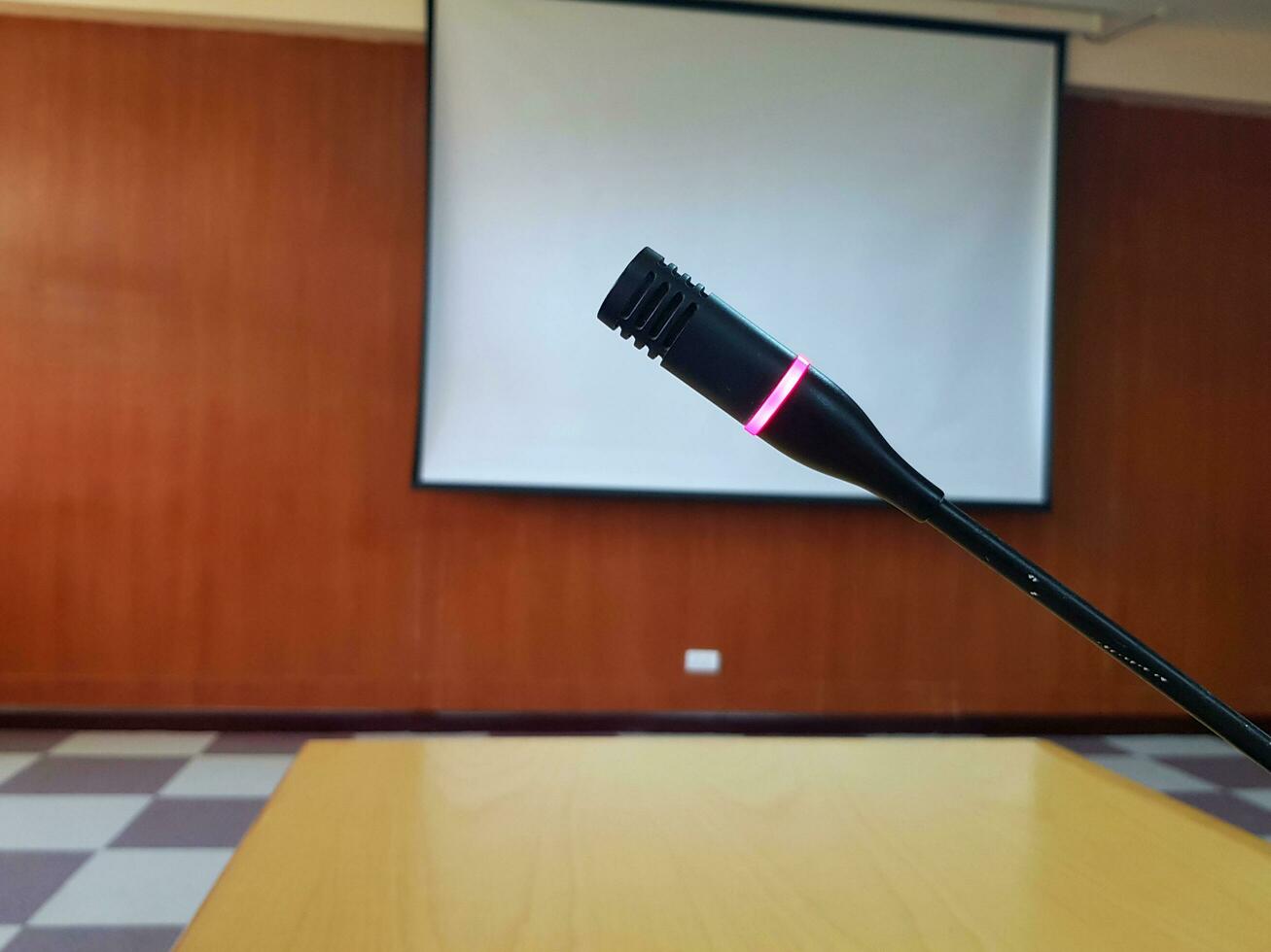 Black Microphone with red light flashing when push button on wooden desk for talking or presentation in conference or meeting room with white projector board blurred background. Device and Tool photo