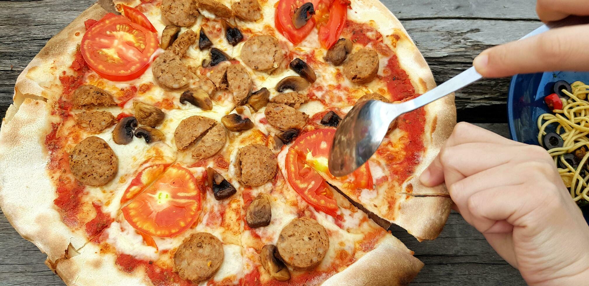 Close up people's hand use spoon and hand eating Pepperoni pizza with  spaghetti and ketchup on wooden table at restaurant. Italian food and Joint party together photo