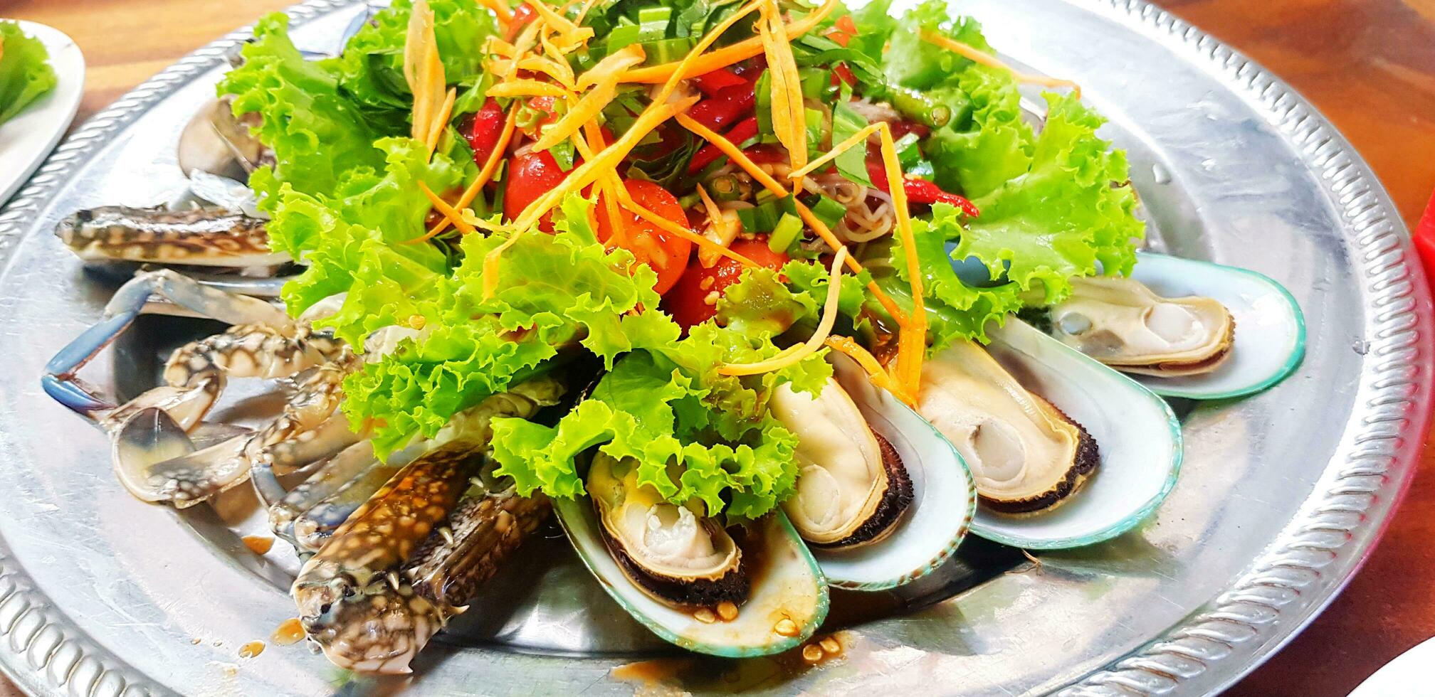 Papaya and vegetable salad with seafood, fresh mussel, prawn and blue crab on stainless steel dish at Thai local restaurant. Healthy life style eating and Diet food concept photo