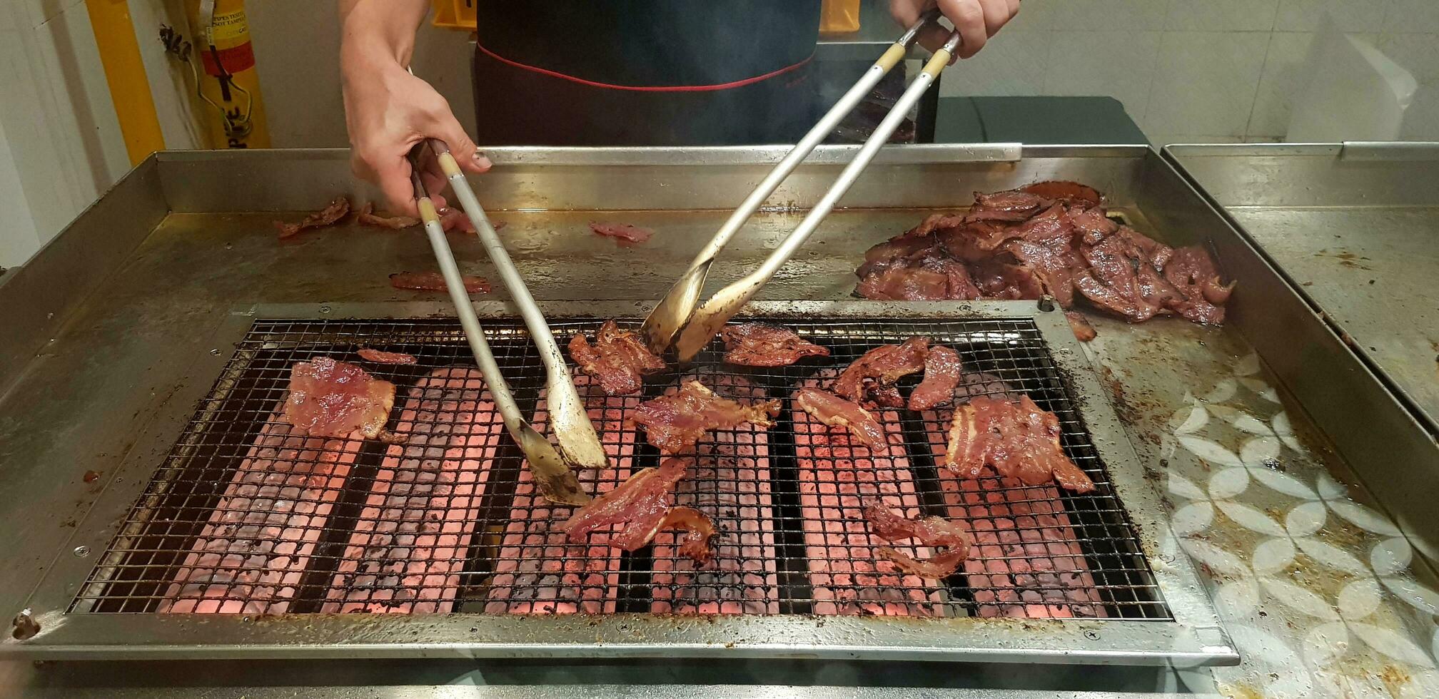 cerca arriba muchos A la parrilla rojo Cerdo o parilla comida en el red estufa con movimiento de del chef mano utilizando utensilio en el cocina a Singapur. selectivo atención y delicioso concepto foto