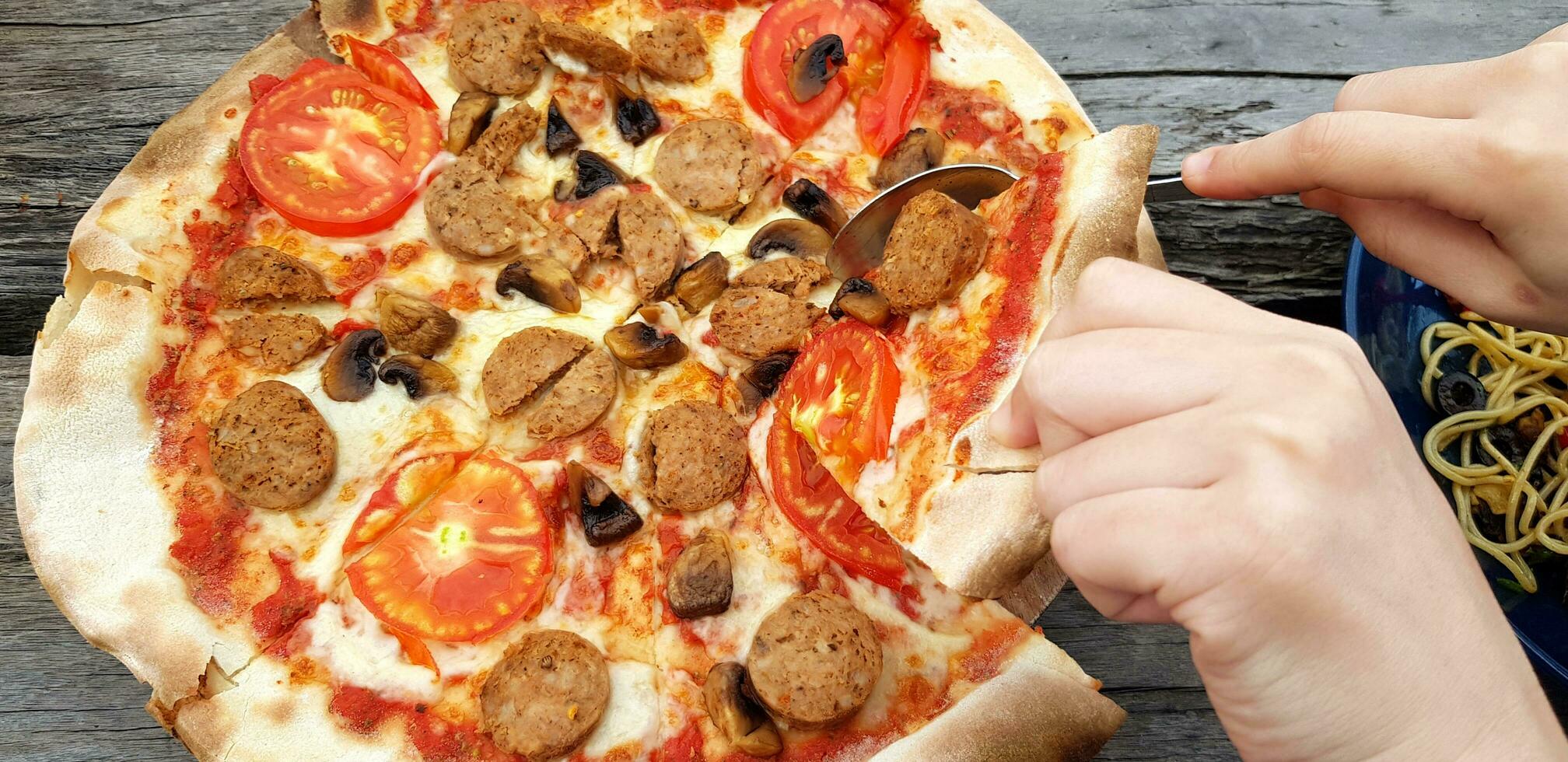 cerca arriba gente mano utilizar cuchara y mano comiendo pepperoni Pizza y espaguetis en de madera mesa a restaurante. italiano comida y articulación fiesta juntos foto