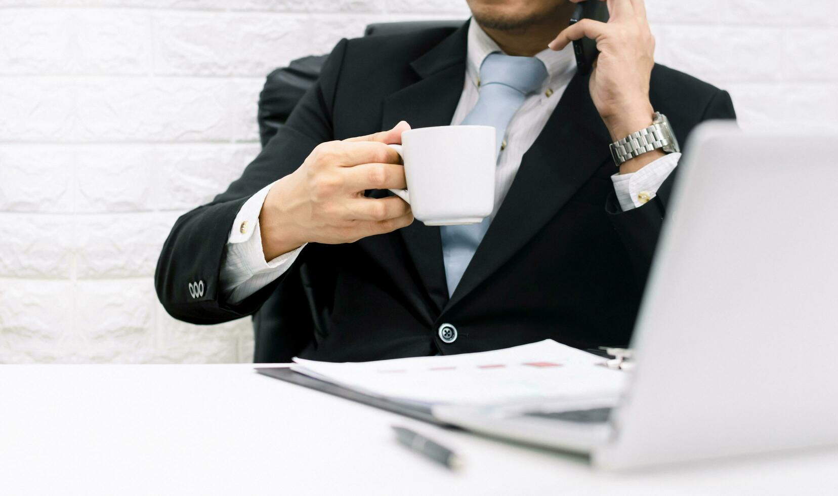 Coffee break businessman executive working relax Hold the phone on laptop at his desk. photo