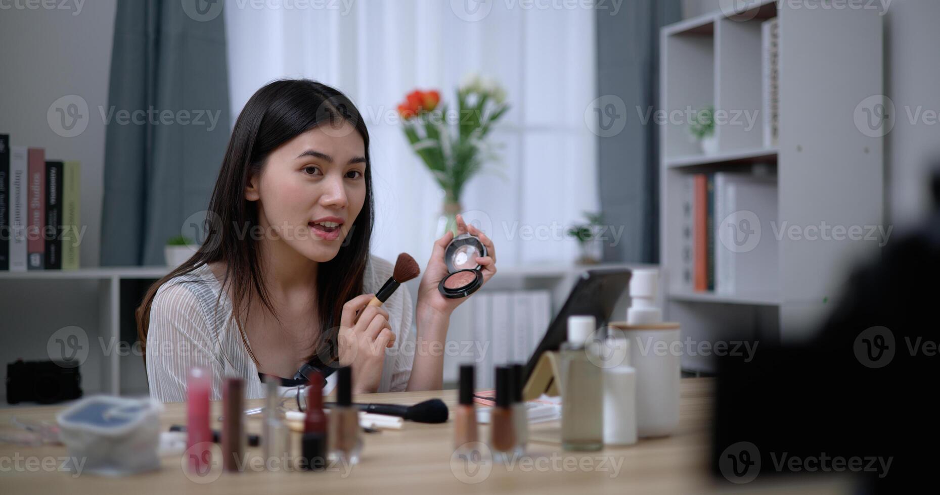 hermosa joven asiático mujer blogger muestra cómo a hacer arriba productos cosméticos a hogar foto