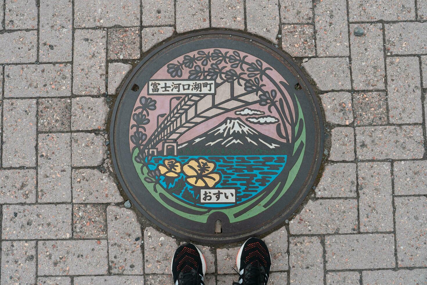KAWAGUCHIKO, JAPAN - APRIL 7, 2023 Top view of manhole cover in Kawaguchiko, Japan with feet standing nearby photo