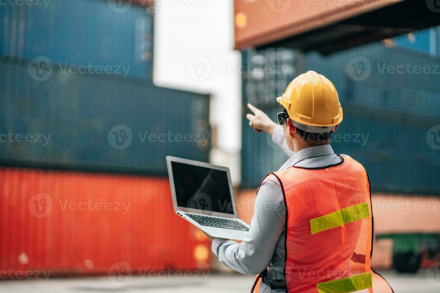 Asian technician dock worker in protective safety jumpsuit uniform and with hardhat and use laptop computer at cargo container shipping warehouse. transportation import,export logistic industrial photo