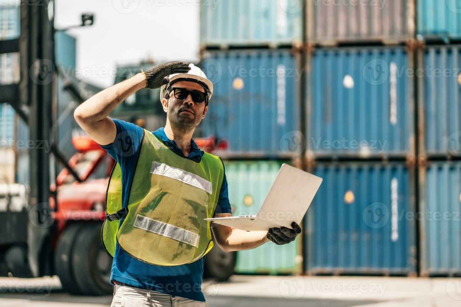 Engineer dock worker in protective safety jumpsuit uniform and with hardhat and use laptop computer at cargo container shipping warehouse. transportation import,export logistic industrial photo