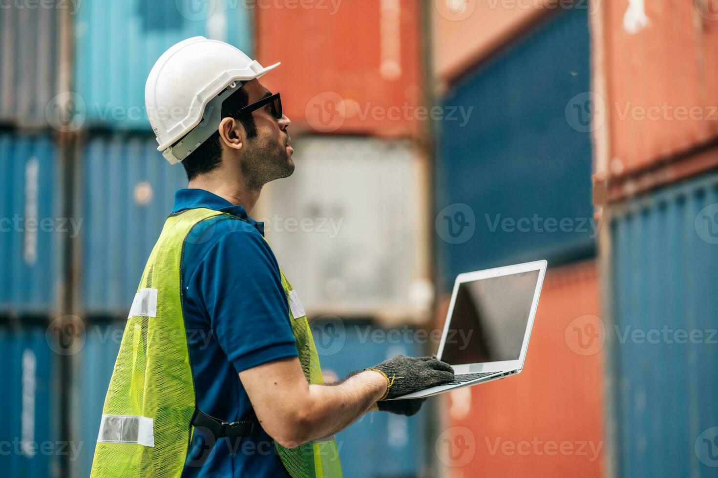 Engineer dock worker in protective safety jumpsuit uniform and with hardhat and use laptop computer at cargo container shipping warehouse. transportation import,export logistic industrial photo