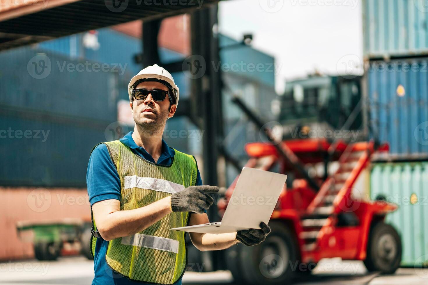 Engineer dock worker in protective safety jumpsuit uniform and with hardhat and use laptop computer at cargo container shipping warehouse. transportation import,export logistic industrial photo