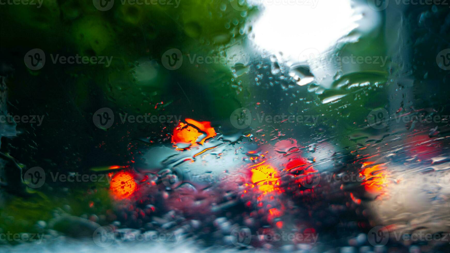 gotas de lluvia en el parabrisas de un coche conducción a lo largo el calle en un soleado tarde foto