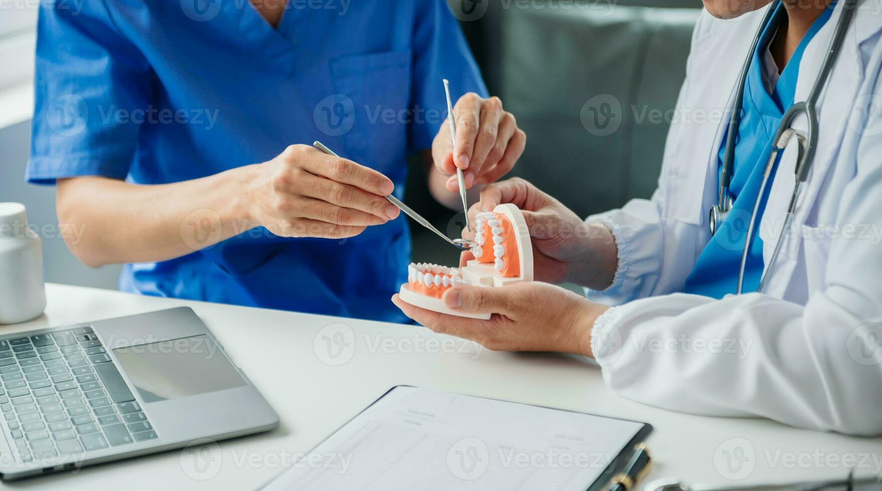 Dentist sitting at table with jaw samples tooth model and working with tablet and laptop in dental office professional dental clinic. medical doctor working photo