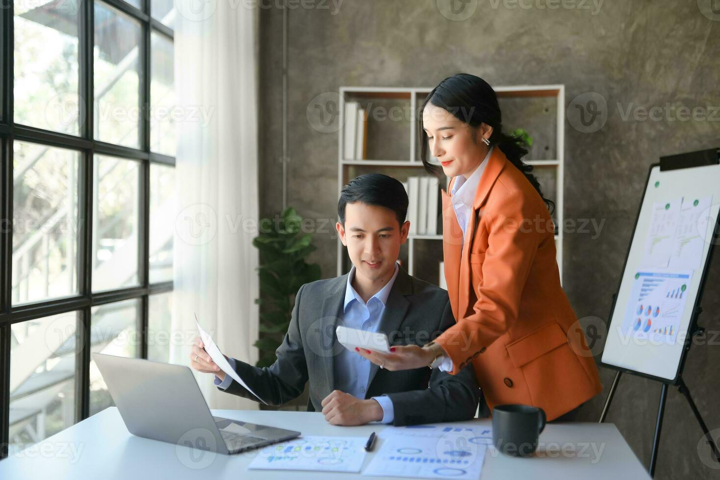 Asian business colleague business presents and explains and using laptop and tablet. Teamwork, financial marketing team, while sitting in office room. photo