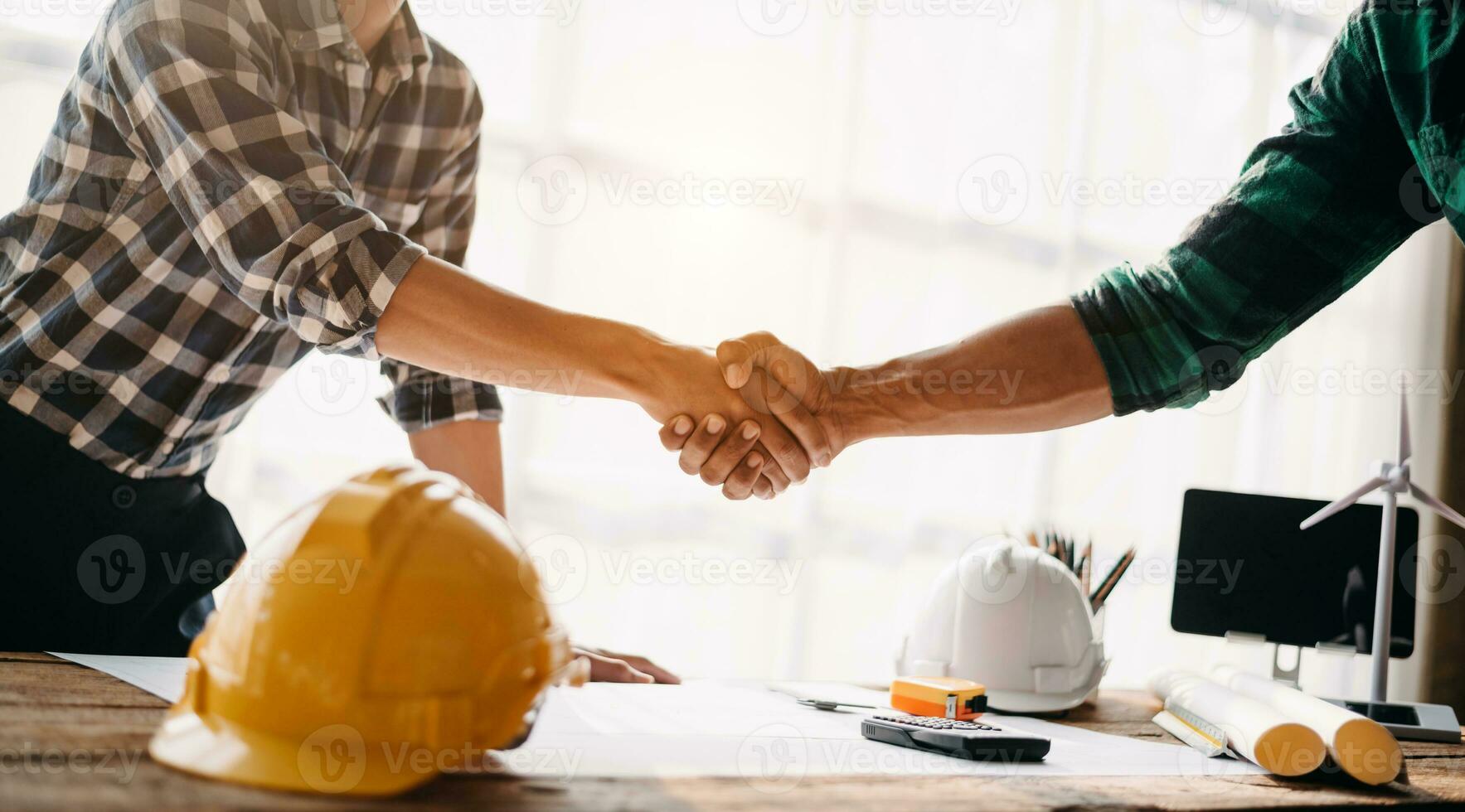 Construction team shake hands greeting start new project plan behind yellow helmet on desk in office center to consults about their building project. in office photo