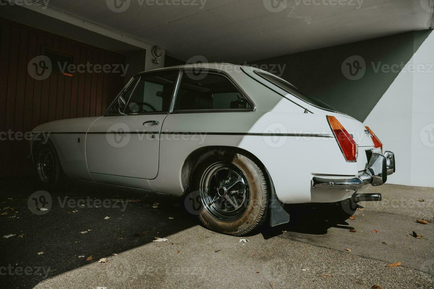 Rear view of the white classic retro sports car parking in the shadow under the house in front of the garage door photo