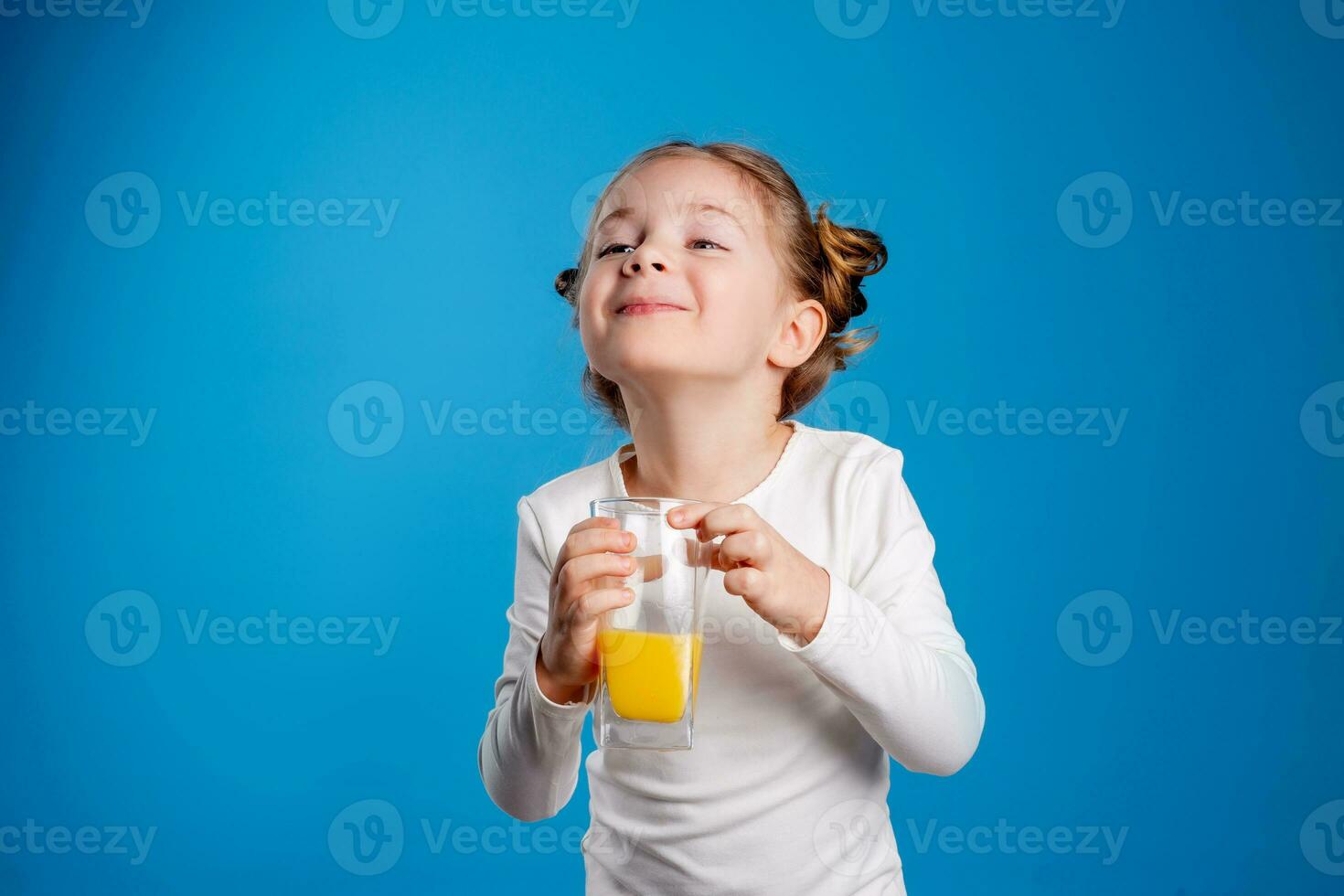 portrait of a little girl of Slavic appearance drinking orange juice on a blue background photo