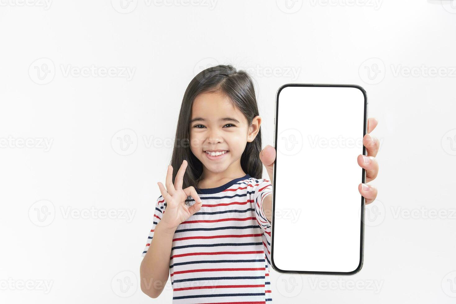 Asian little girl holding smartphone mockup of blank screen and smiling on white background. photo