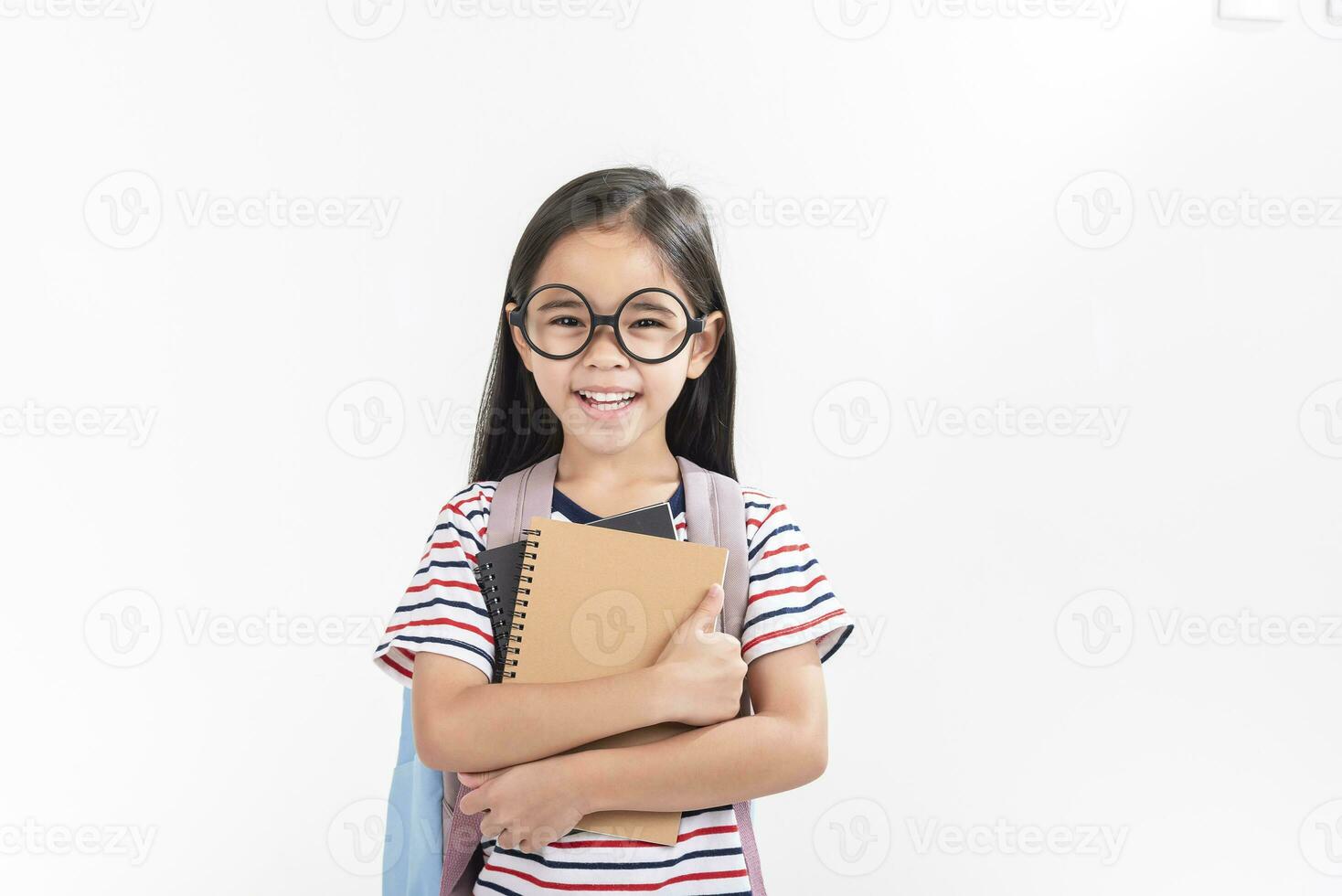 schoolgirl hugging book wearing backpack smiling isolated on white background photo