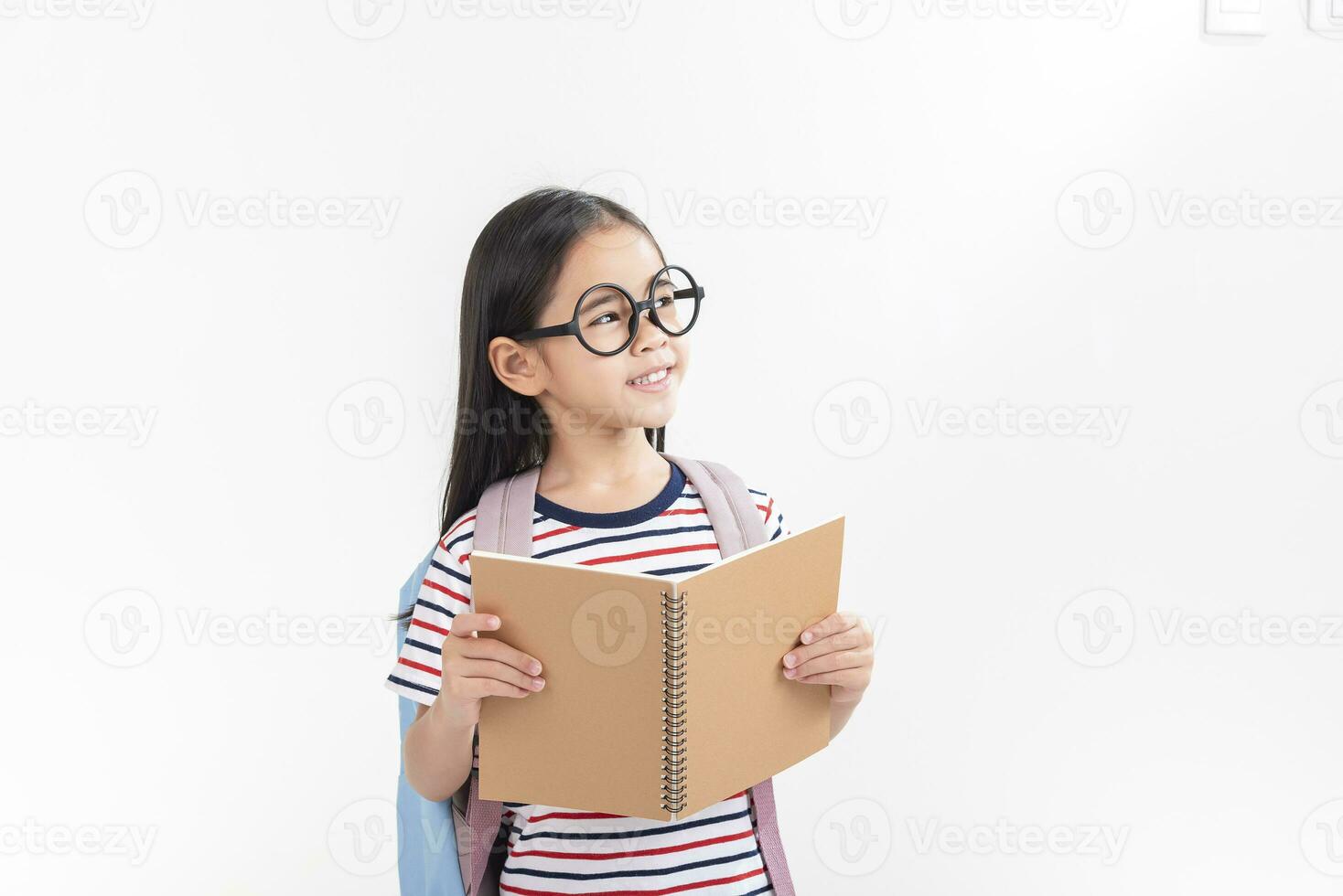 schoolgirl hugging book wearing backpack smiling isolated on white background photo