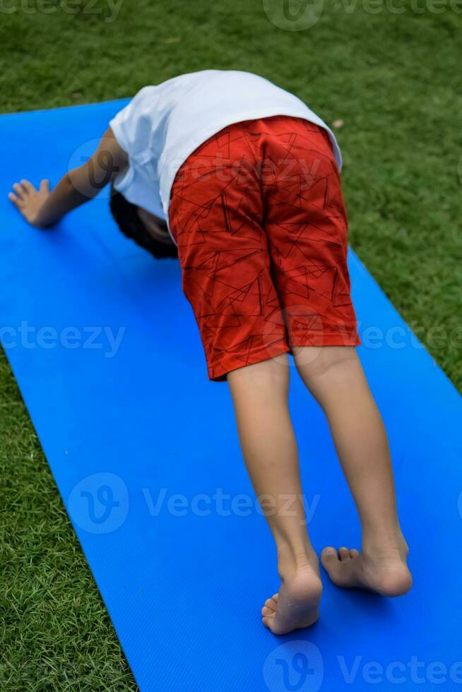 Asian smart kid doing yoga pose in the society park outdoor, Children's yoga pose. The little boy doing Yoga and meditation exercise. photo