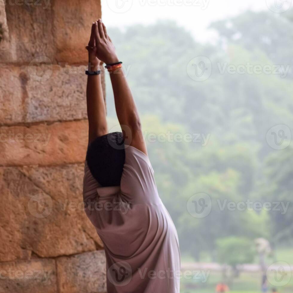 Inspired Indian young man doing yoga asanas in Lodhi Garden Park, New Delhi, India. Young citizen exercising outside and standing in yoga side angle pose. Fitness outdoors and life balance concept photo