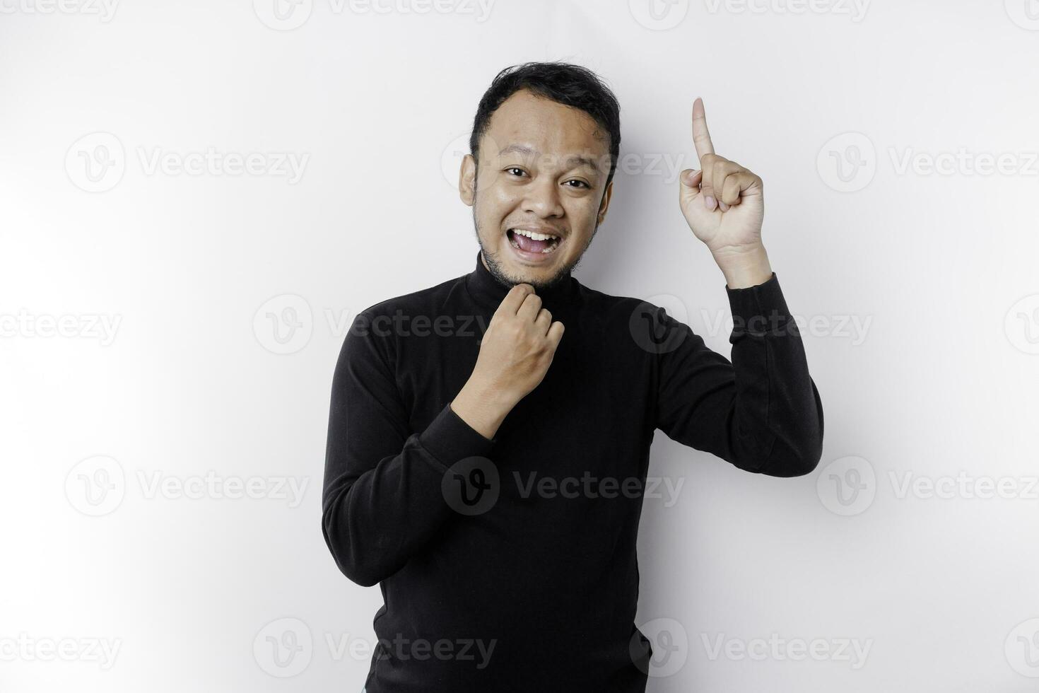 A thoughtful young man wearing a black shirt while looking and pointing at copy space above him, isolated by white background photo
