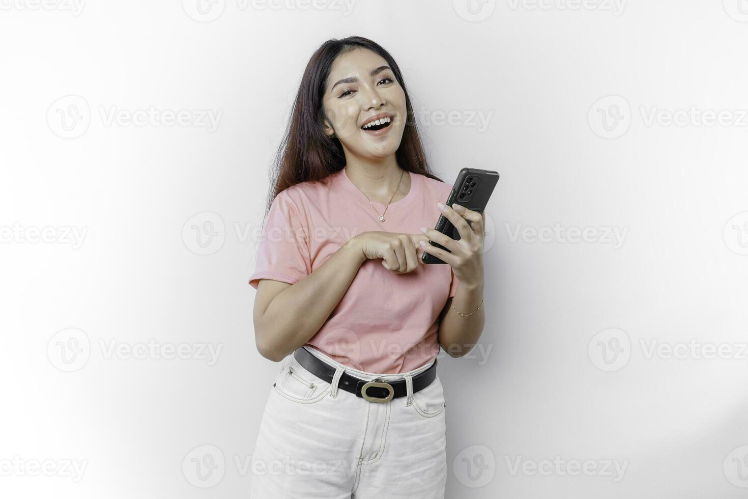 A portrait of a happy Asian woman is wearing pink t-shirt and holding her phone, isolated by white background photo