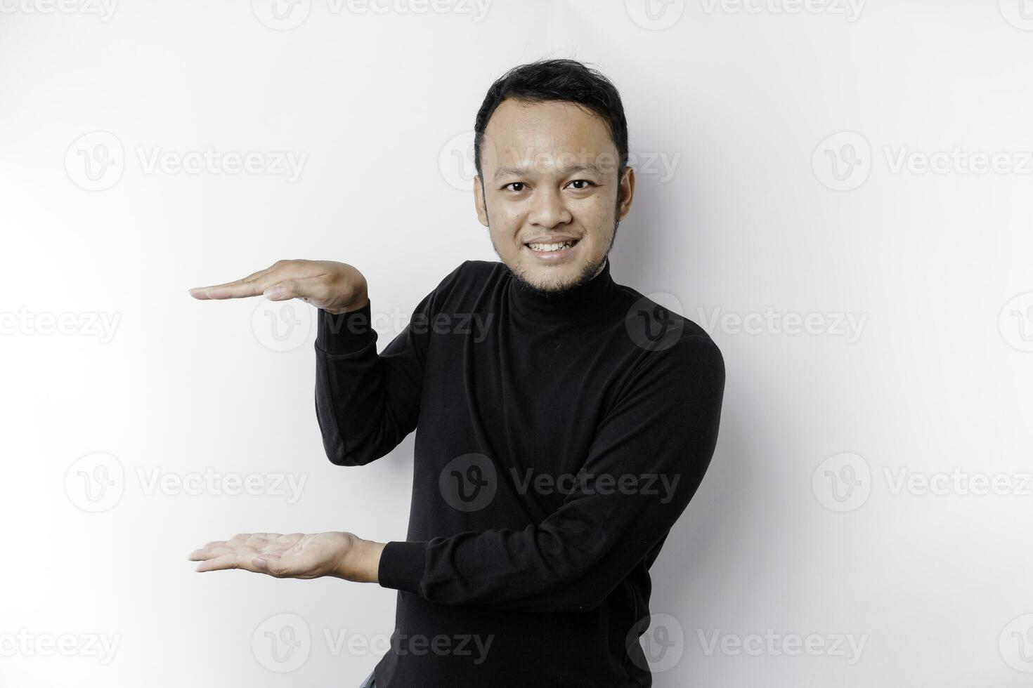 Smiling young Asian man is standing over isolated background holding copy space imaginary on the palm to insert an ad photo