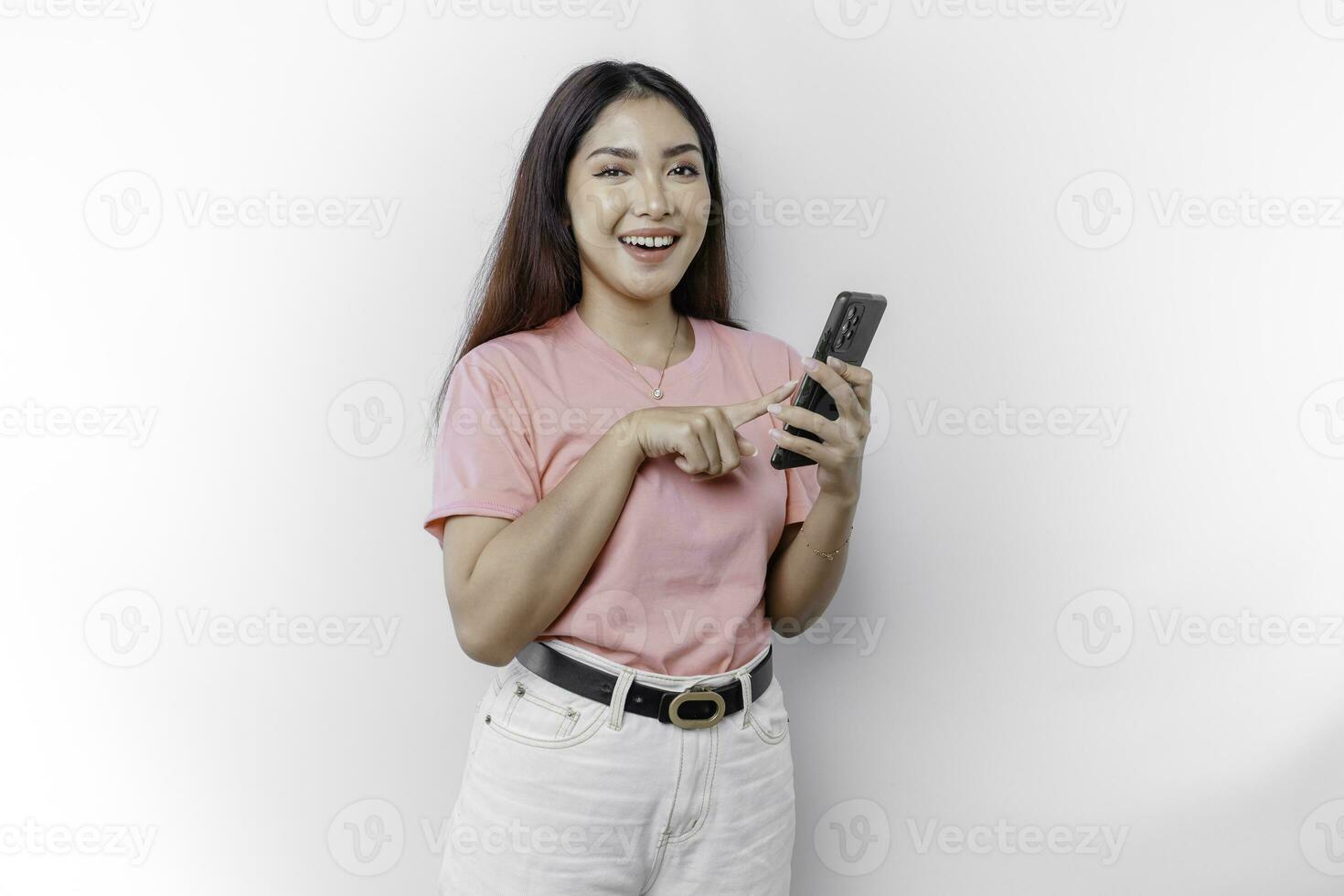 A portrait of a happy Asian woman is wearing pink t-shirt and holding her phone, isolated by white background photo