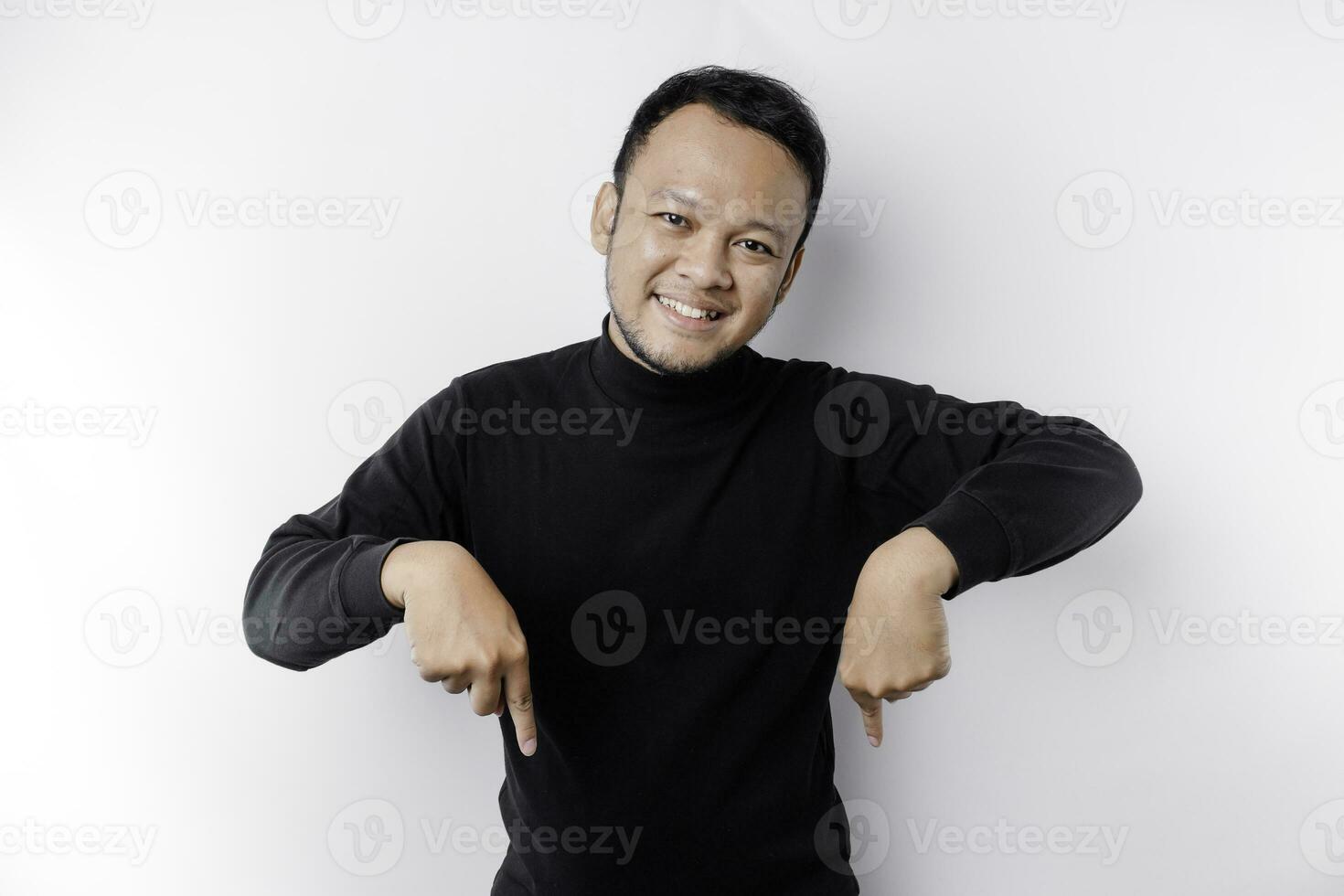 Excited Asian man wearing black shirt pointing at the copy space below him, isolated by white background photo