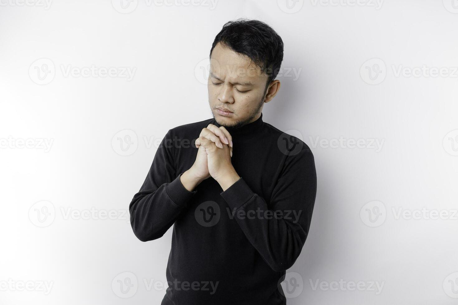 Religious Asian man wearing a black shirt praying to God, isolated by a white background photo