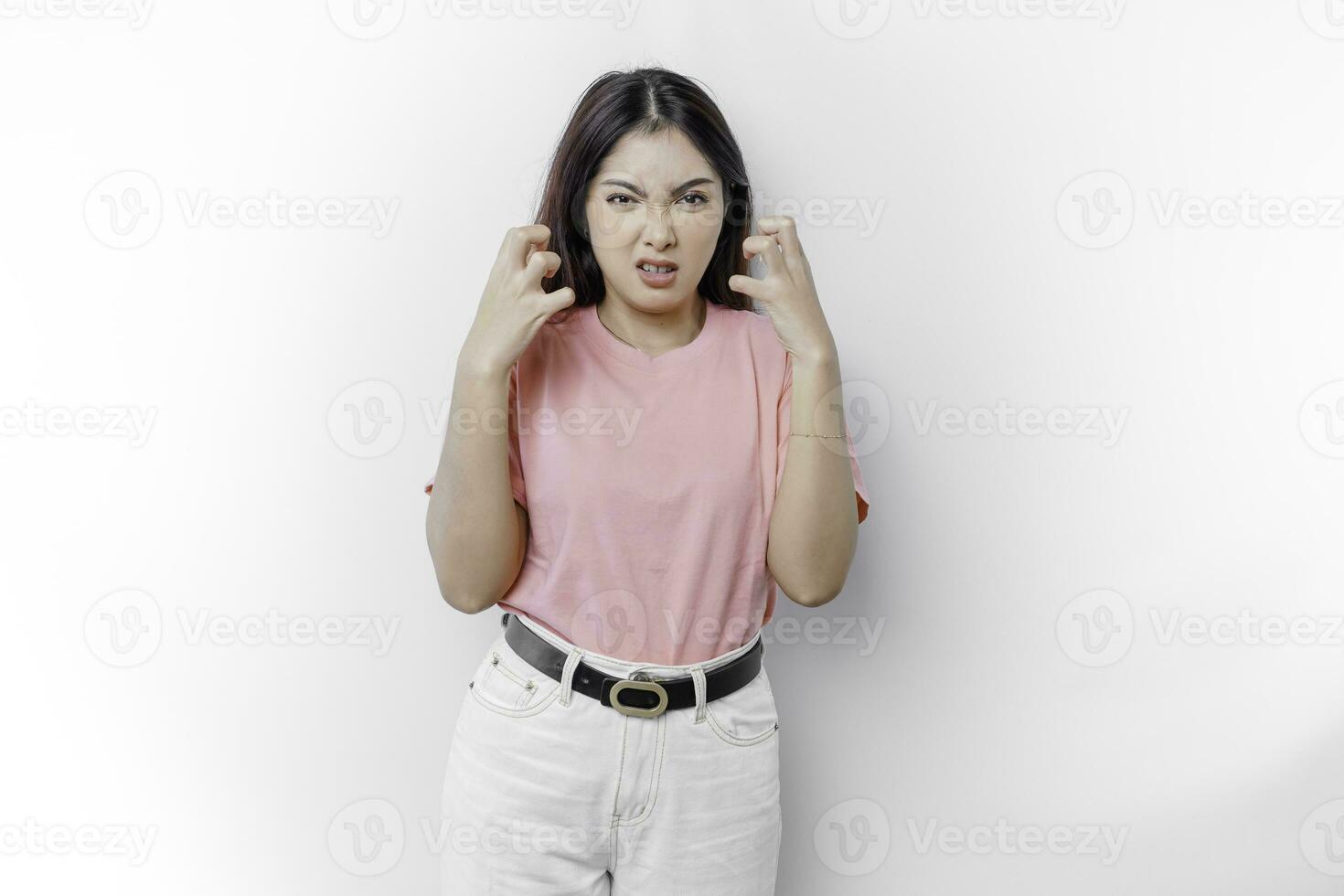 A dissatisfied young Asian woman looks at the camera posing on a white background, disgruntled girl with irritated face expressions show negative attitude concept image photo
