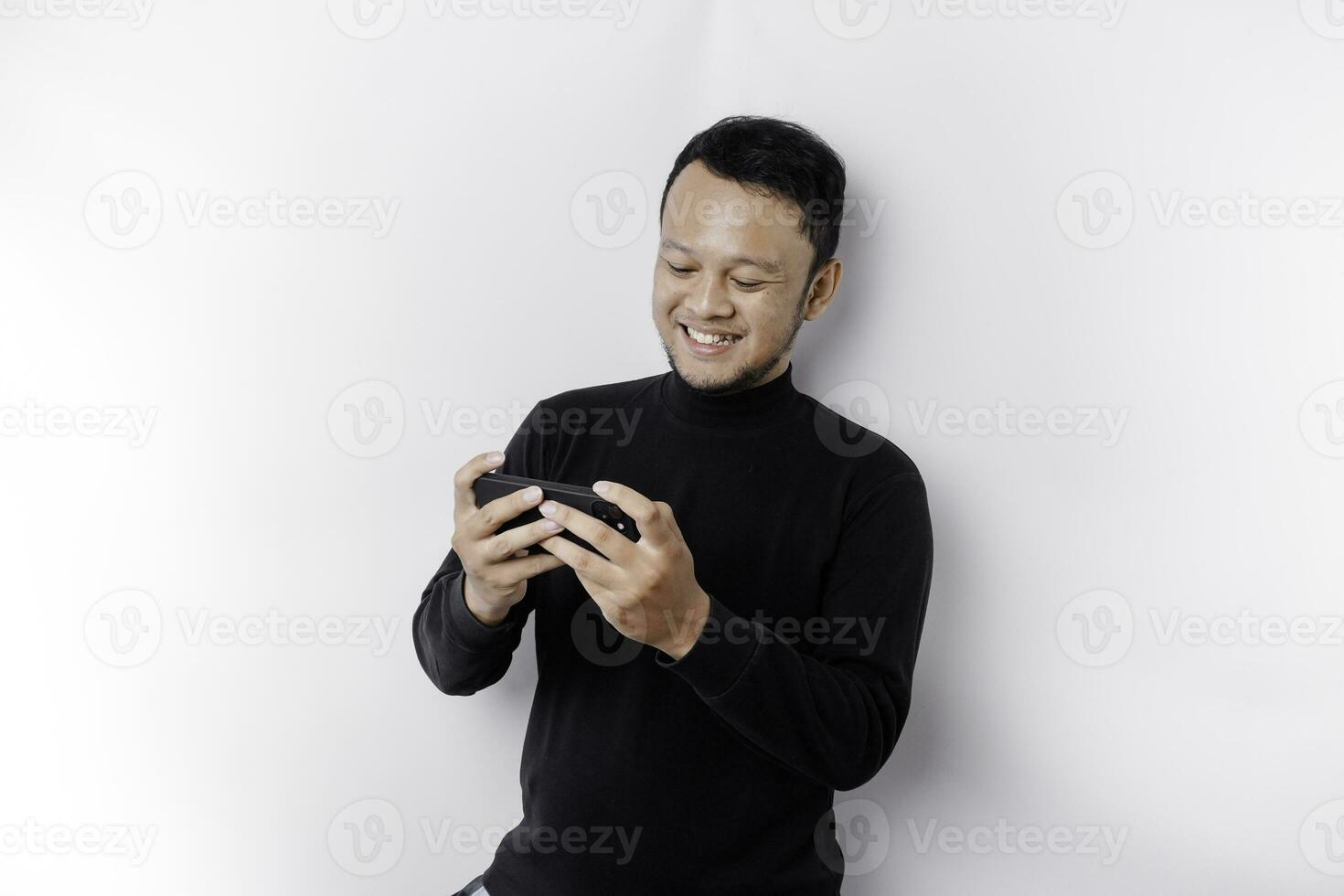 joven asiático hombre en casual vestir es jugando juegos con móvil teléfono con un blanco antecedentes aislado. foto