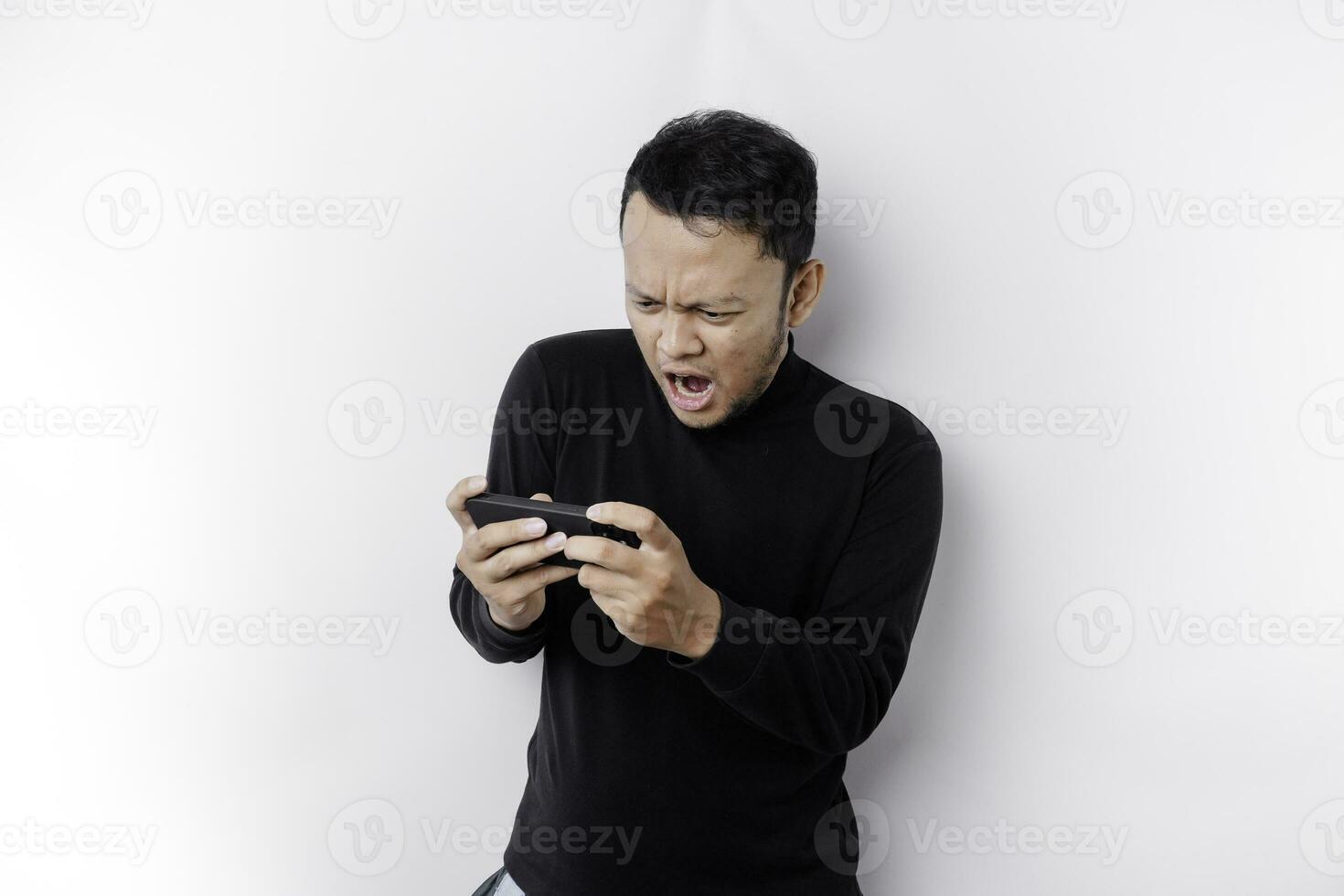 Young Asian man in casual wear is playing games with mobile phone with a white background isolated. photo