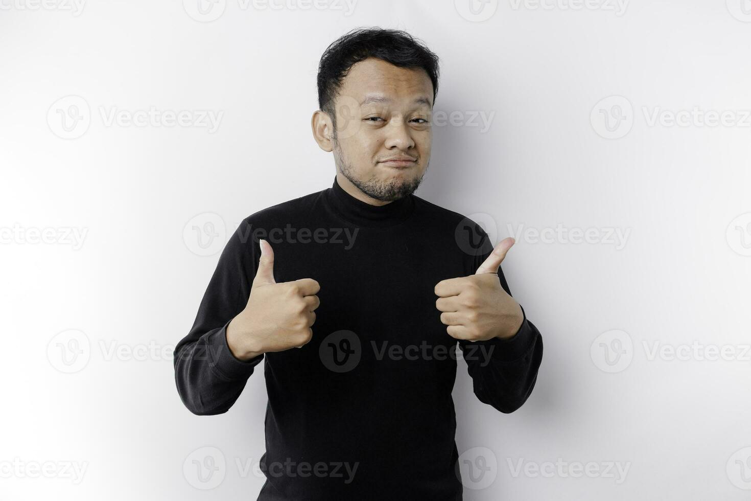 Excited Asian man wearing black shirt gives thumbs up hand gesture of approval, isolated by white background photo