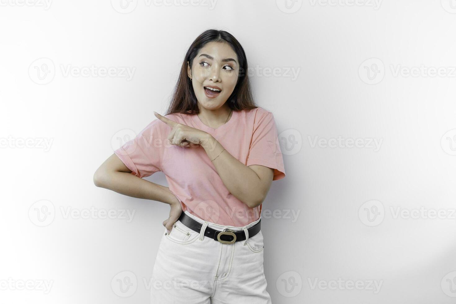 conmocionado asiático mujer vistiendo rosado camiseta, señalando a el Copiar espacio en junto a su, aislado por blanco antecedentes foto