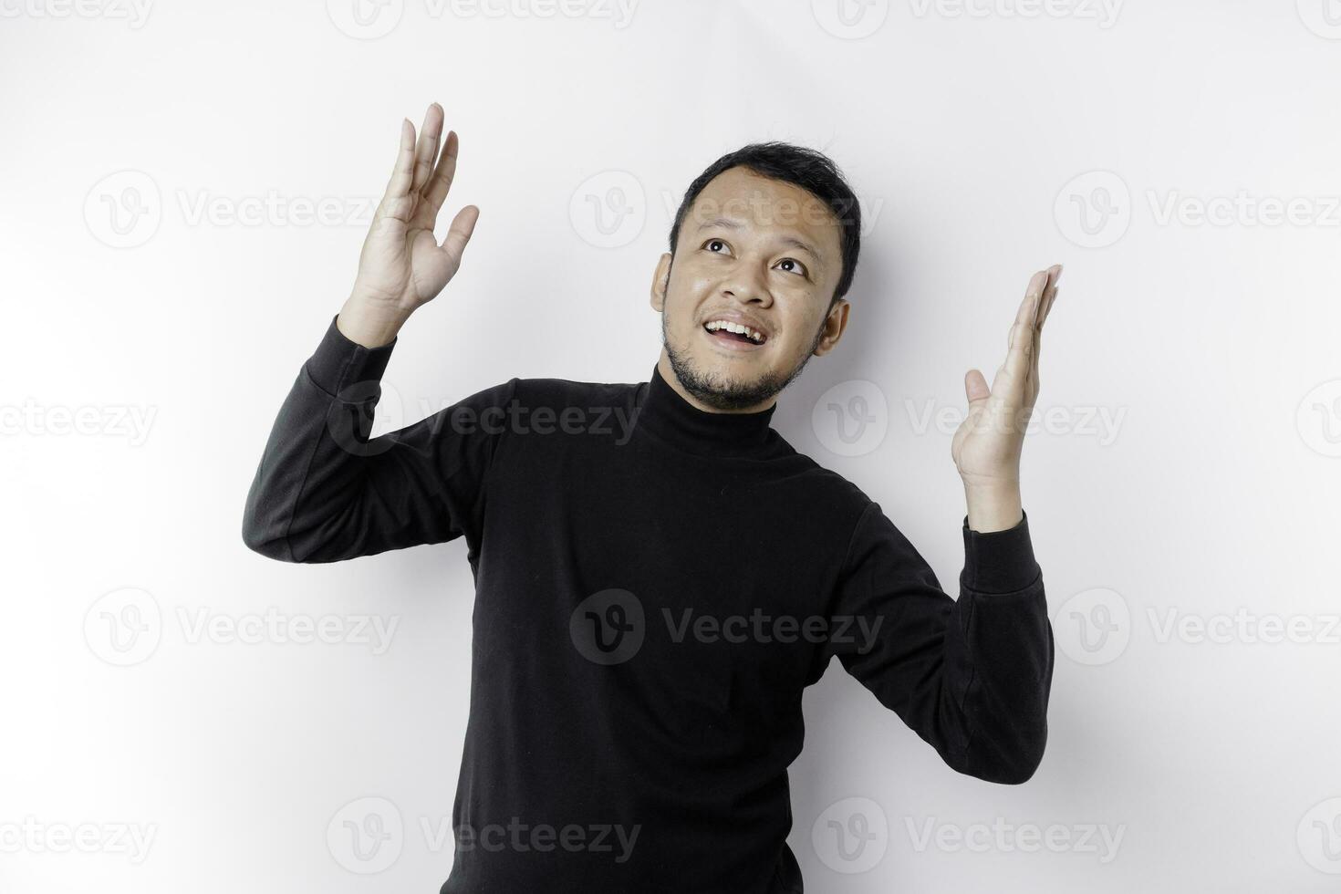Excited Asian man wearing black shirt pointing at the copy space on top of him, isolated by white background photo