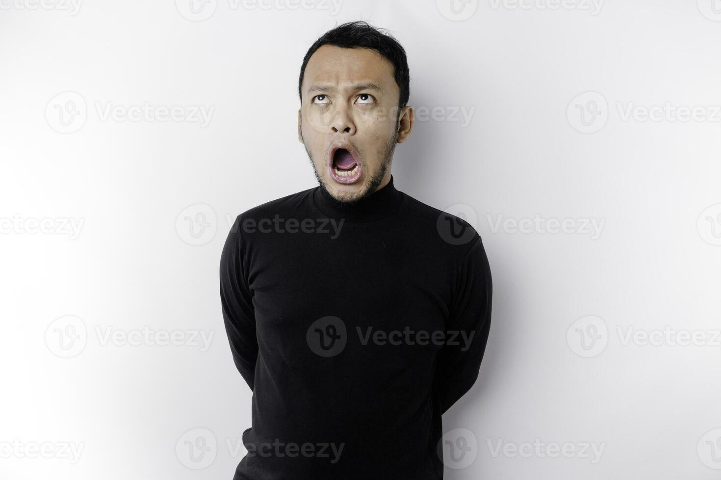 Shocked Asian man with his mouth wide open wearing black shirt, isolated by a white background photo