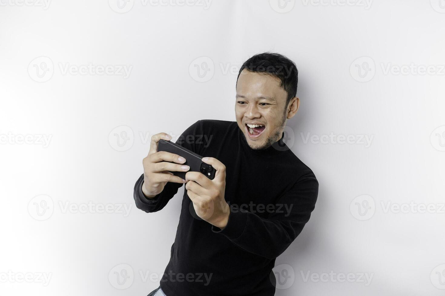 joven asiático hombre en casual vestir es jugando juegos con móvil teléfono con un blanco antecedentes aislado. foto