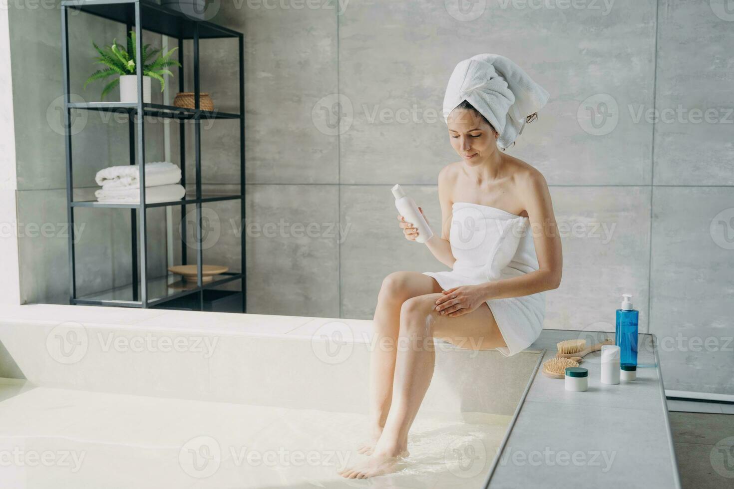 Female massaging leg using natural anticellulite skincare cosmetics in bathroom. Body care treatment photo