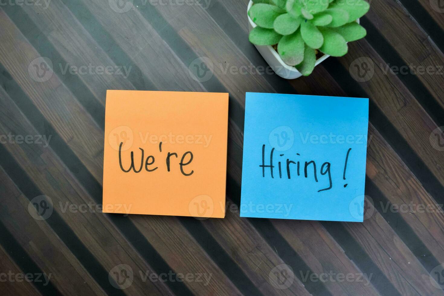 Concept of We're Hiring write on sticky notes isolated on Wooden Table. photo