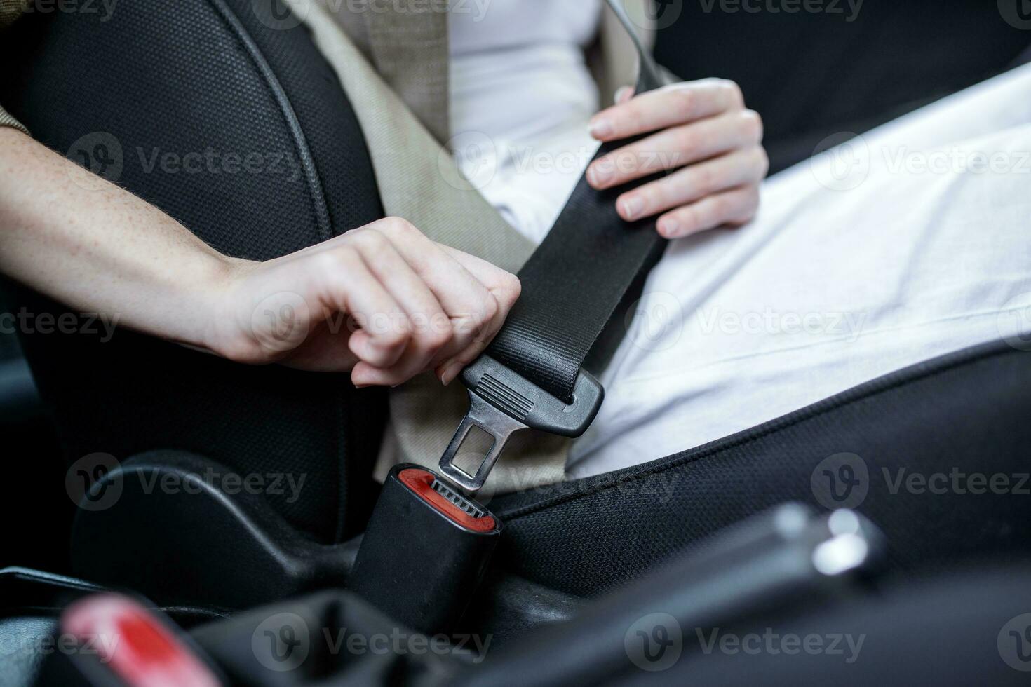 cropped view of woman fastening safety belt while sitting in car on blurred foreground. Cut view of young woman's hands locking seat belt in car. Sitting alone. Close up photo