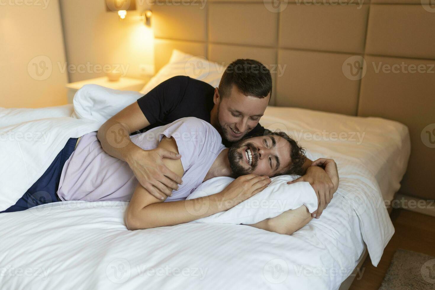 Gay couple embracing each other with their eyes closed. Two young male lovers touching their faces together while lying in bed in the morning. Affectionate young gay couple bonding at home. photo