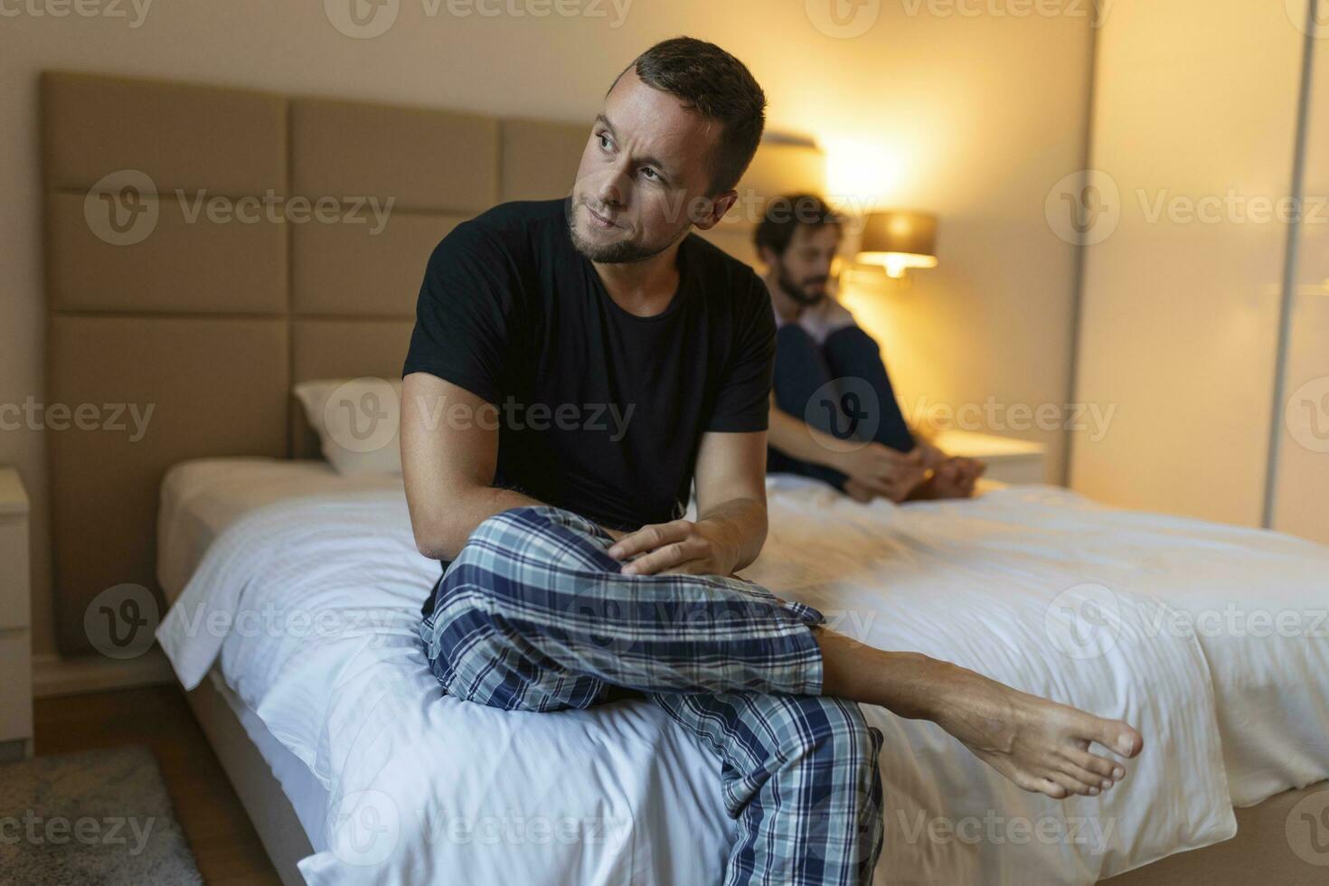 Frustrated sad boyfriend sit on bed think of relationship problems, thoughtful gay couple after quarrel lost in thoughts, upset lovers consider break up, offended person disappointed by boyfriend photo