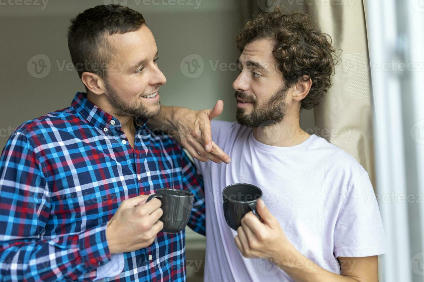 Young gay couple in love looking out the window. Two young androgynous men smiling together and having coffee. photo