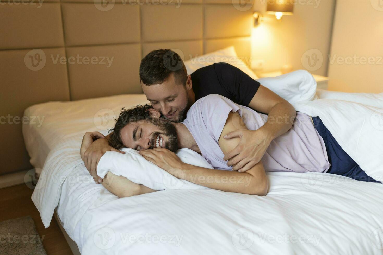 Gay couple embracing each other with their eyes closed. Two young male lovers touching their faces together while lying in bed in the morning. Affectionate young gay couple bonding at home. photo