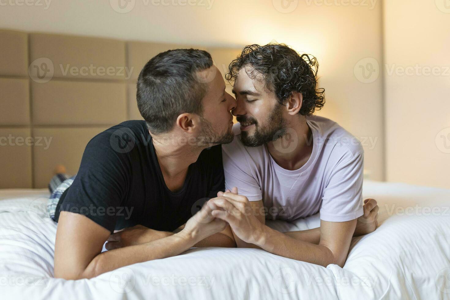 Happy gay couple lying down on the bed at home, hugging and flirting. LGBT gay couple love moments happiness concept photo