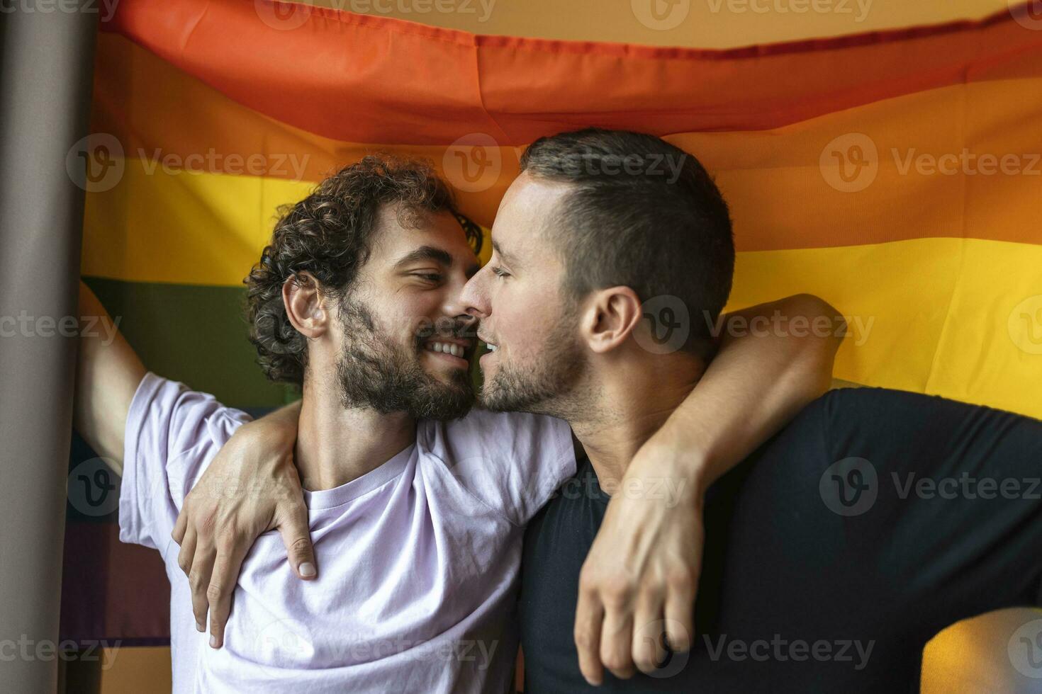 apasionado gay Pareja haciendo fuera con lgbtq bandera en el antecedentes. joven gay Pareja unión afectuosamente adentro. foto