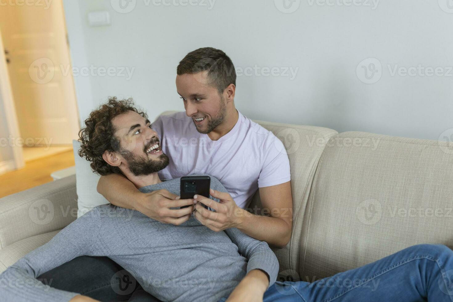 linda joven gay Pareja vídeo vocación su amigos en su vivo habitación a hogar. dos masculino amantes sonriente alegremente mientras saludo su amigos en un teléfono inteligente joven gay Pareja sentado juntos. foto