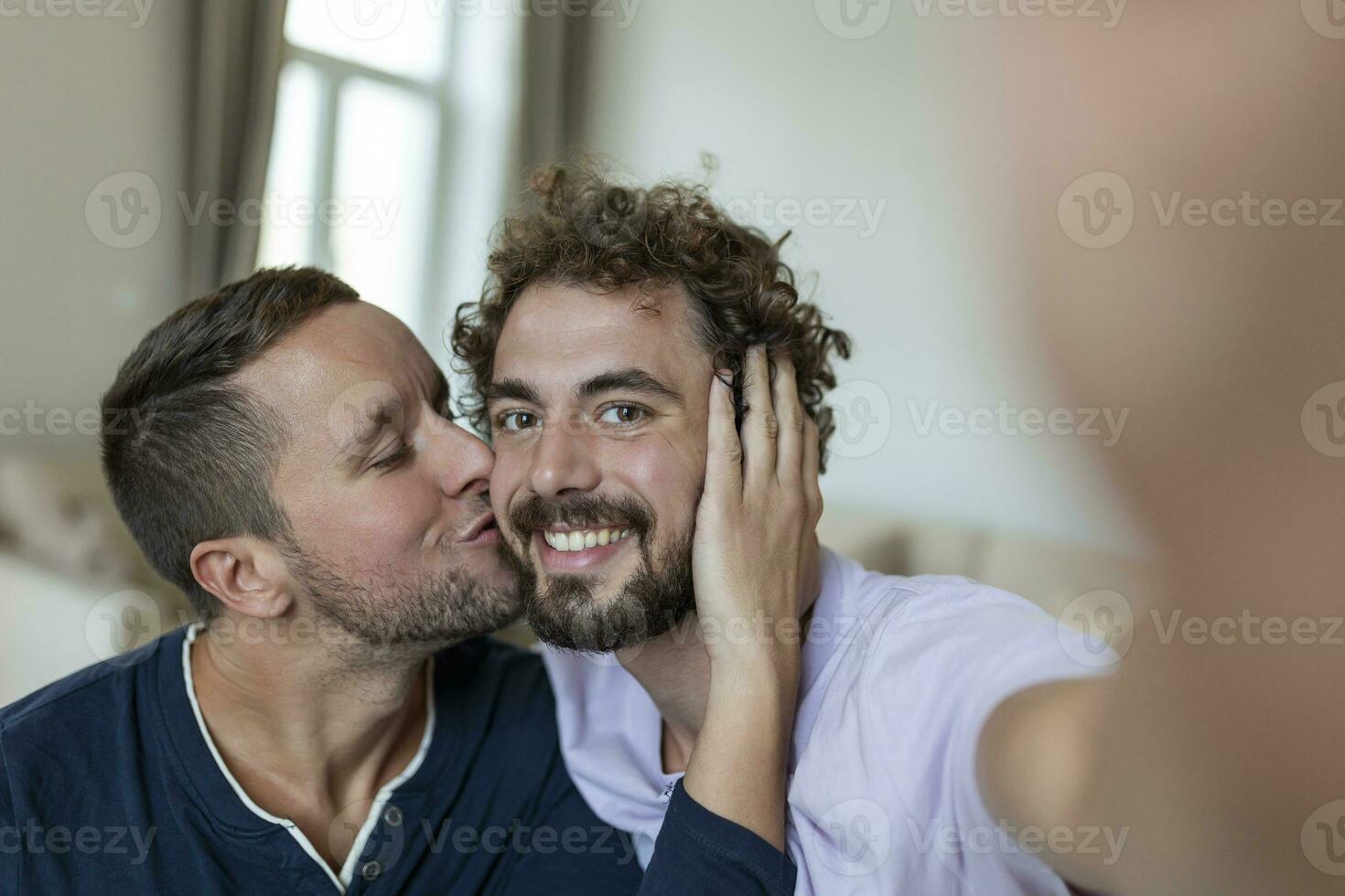 hermoso gay hombre sentado juntos a hogar tomando selfie con móvil teléfono. gay hombre con su compañero sentado por tomando un yo retrato utilizando inteligente teléfono. foto