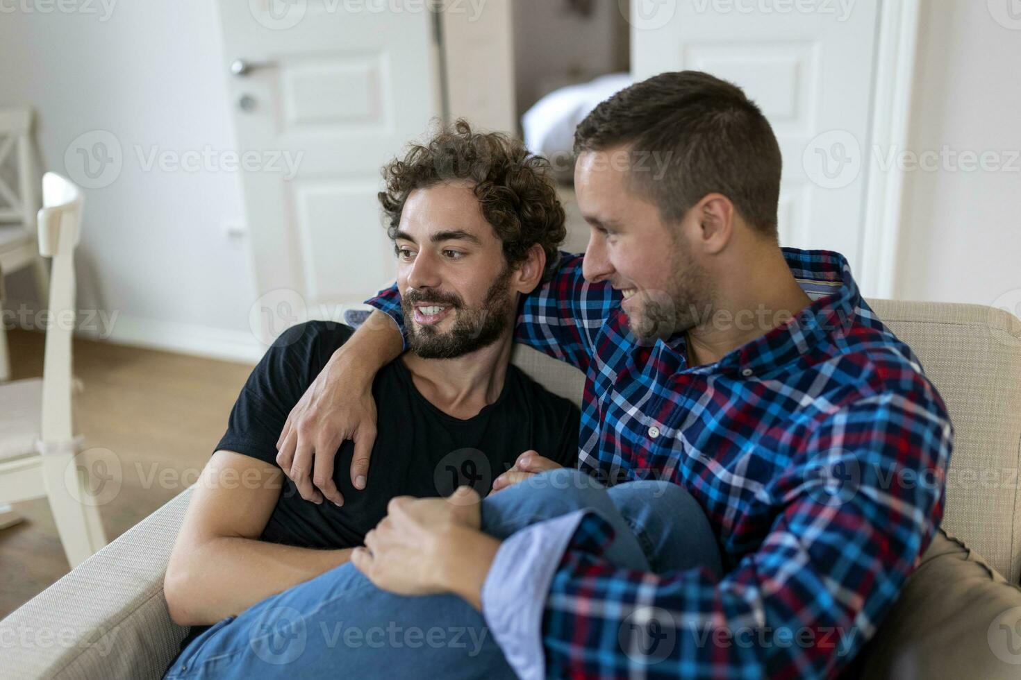 alegre joven gay Pareja sentado juntos. dos cariñoso masculino amantes sonriente alegremente mientras abrazando cada otro. joven gay cupé siendo romántico. foto