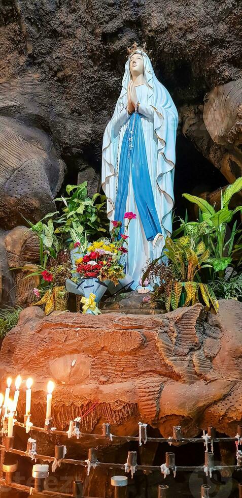 Statue of Holy Virgin Mary in Roman Catholic Church, in the cave of virgin mary, in a rock cave chapel Catholic Church with tropical flowers around photo